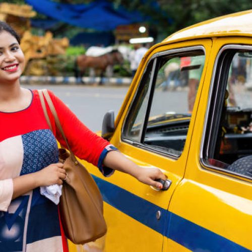 Young Indian woman opening gate of old yellow taxi on road